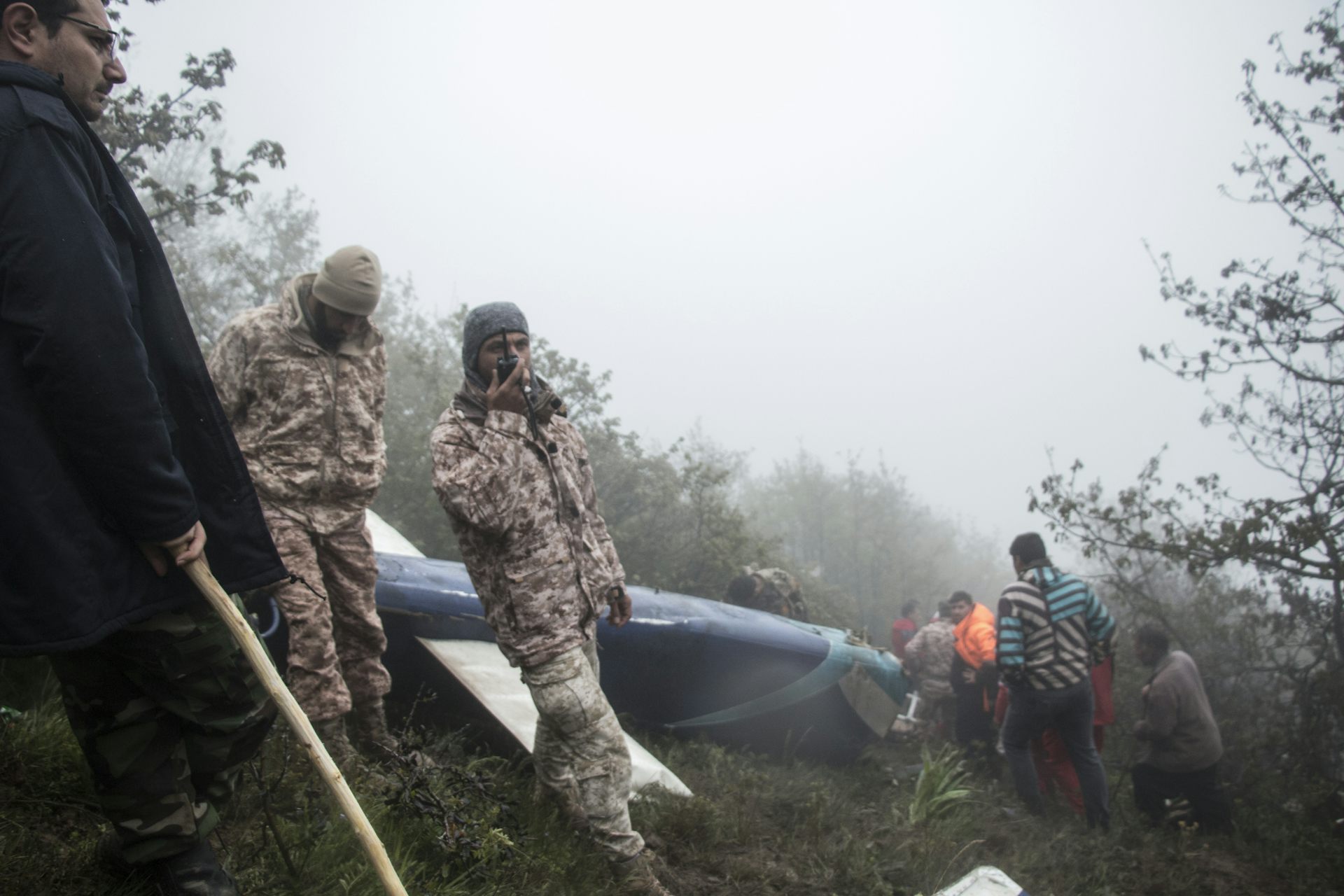 A rescue worker talking into a radio in front of a helicopter wreckage. 