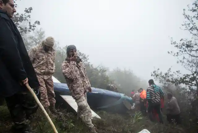 A rescue worker talking into a radio in front of a helicopter wreckage.
