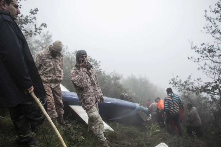 A rescue worker talking into a radio in front of a helicopter wreckage.