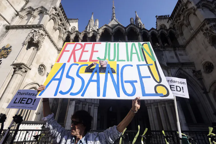 A man holds up a large sign reading FREE JULIAN ASSANGE