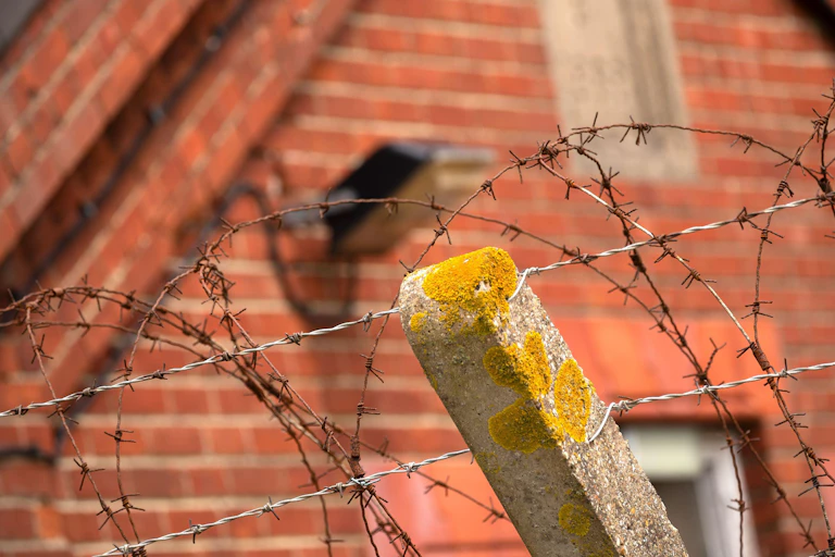 Close up of barbed wire fencing in front of a red brick barracks building