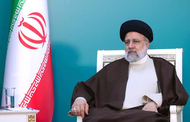 Um homem com trajes tradicionais iranianos senta-se em uma cadeira.