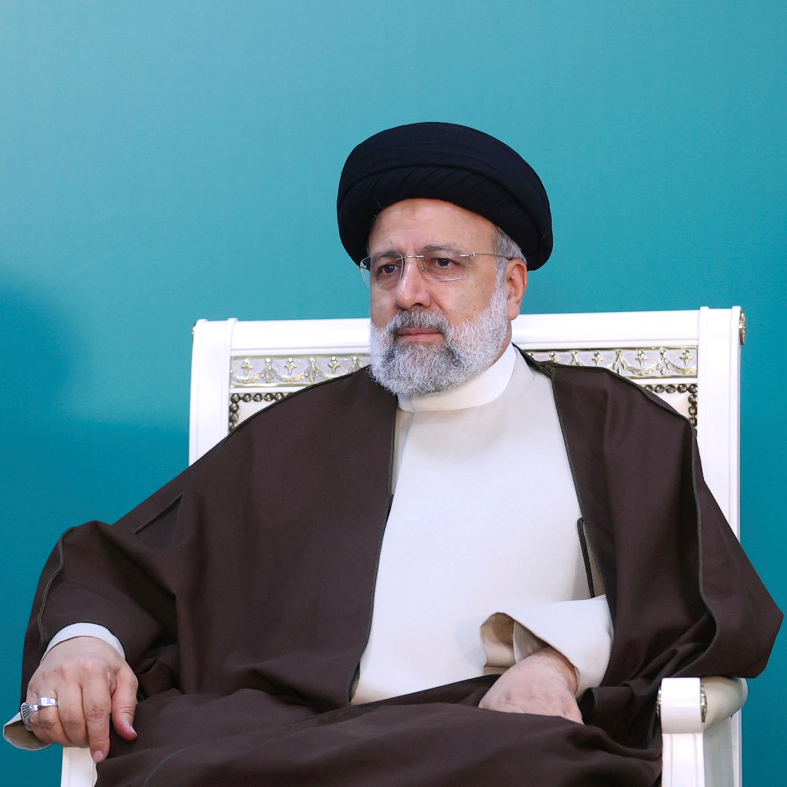 Um homem com trajes tradicionais iranianos senta-se em uma cadeira.