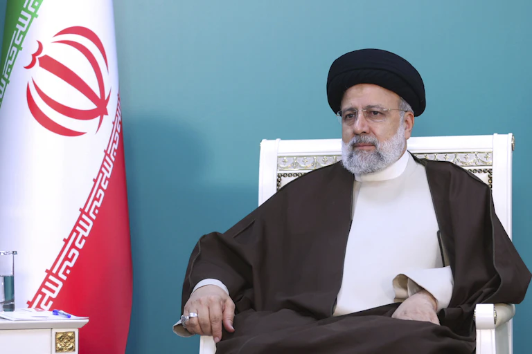 Um homem com trajes tradicionais iranianos senta-se em uma cadeira.