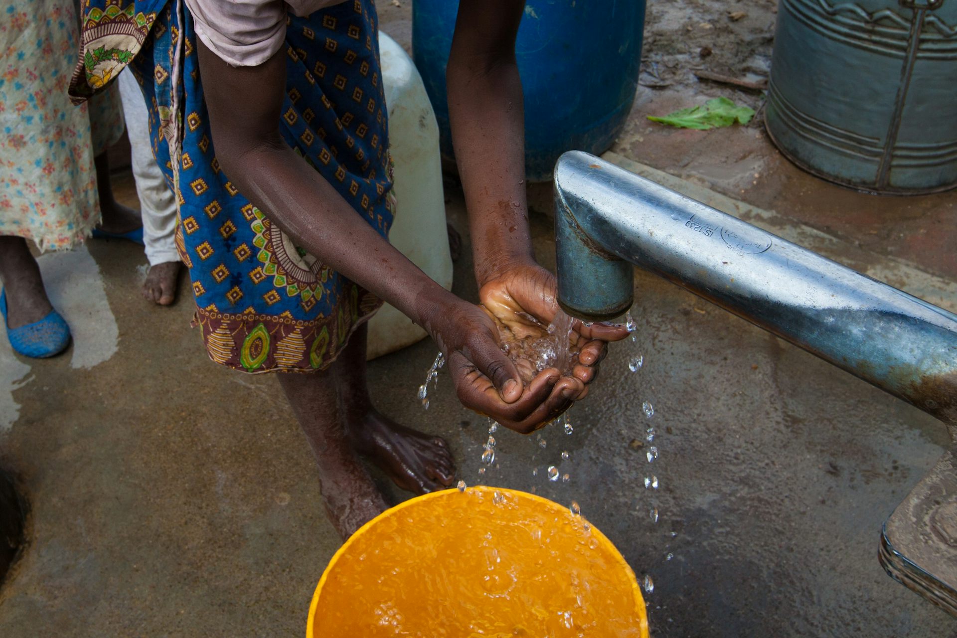 Two arms of a girl washing her hands at a borehole pipe