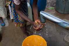 Two arms of a girl washing her hands at a borehole pipe