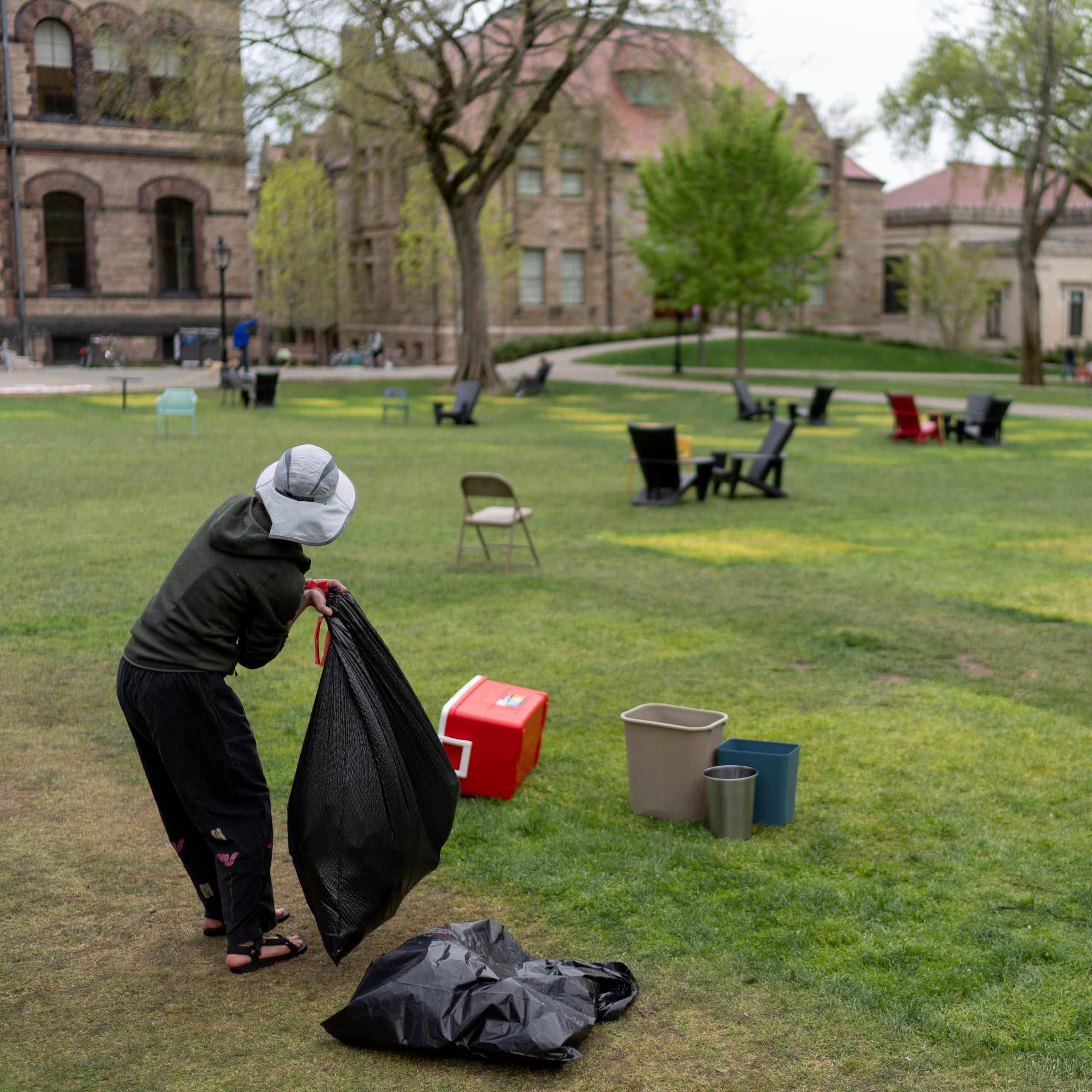 A person wearing a hat puts items in a plastic garbage bag.