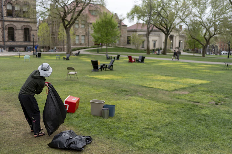 A person wearing a hat puts items in a plastic garbage bag.