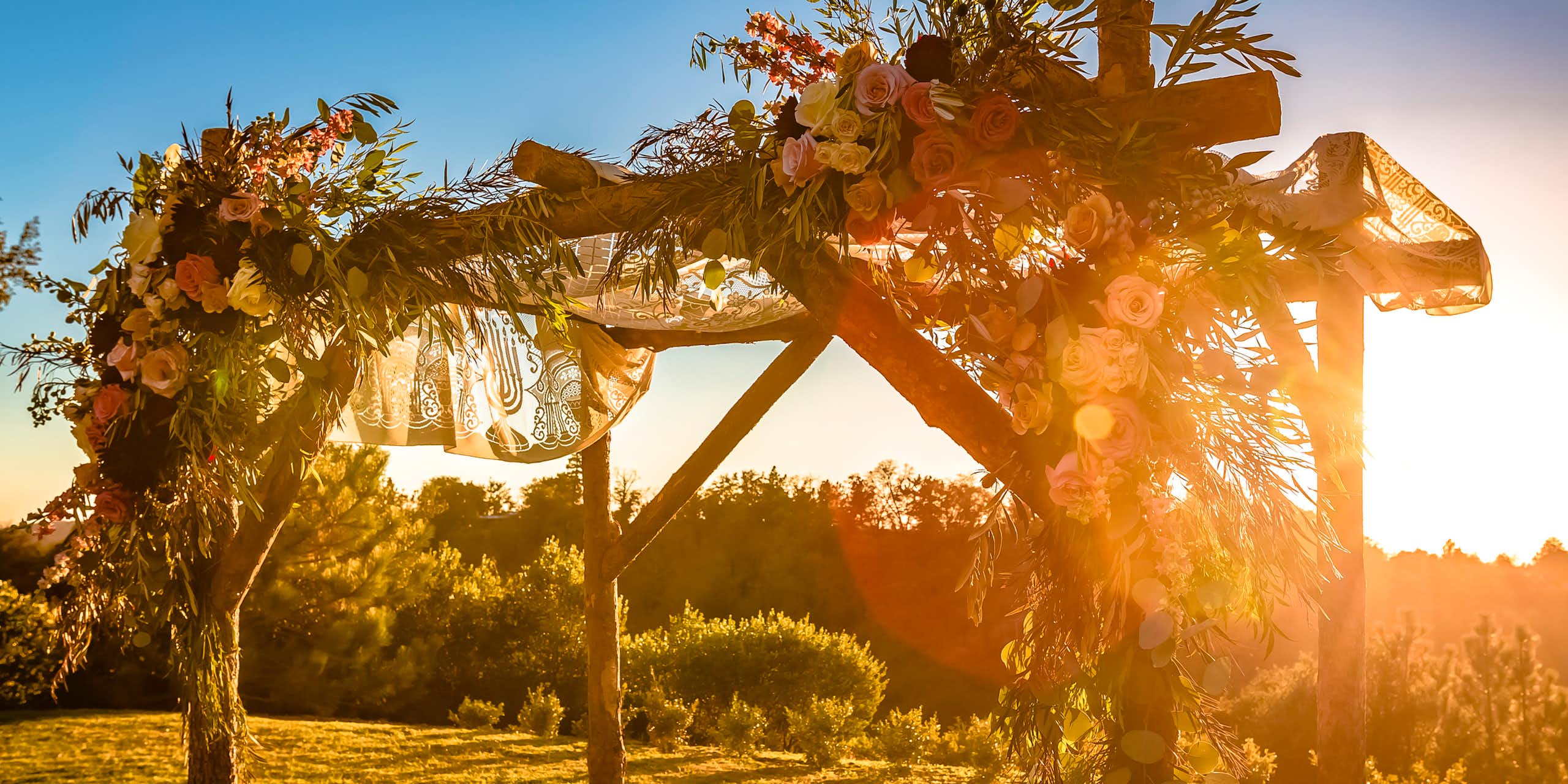 The sun begins to set hazily behind a simple wooden canopy adorned with flowers.