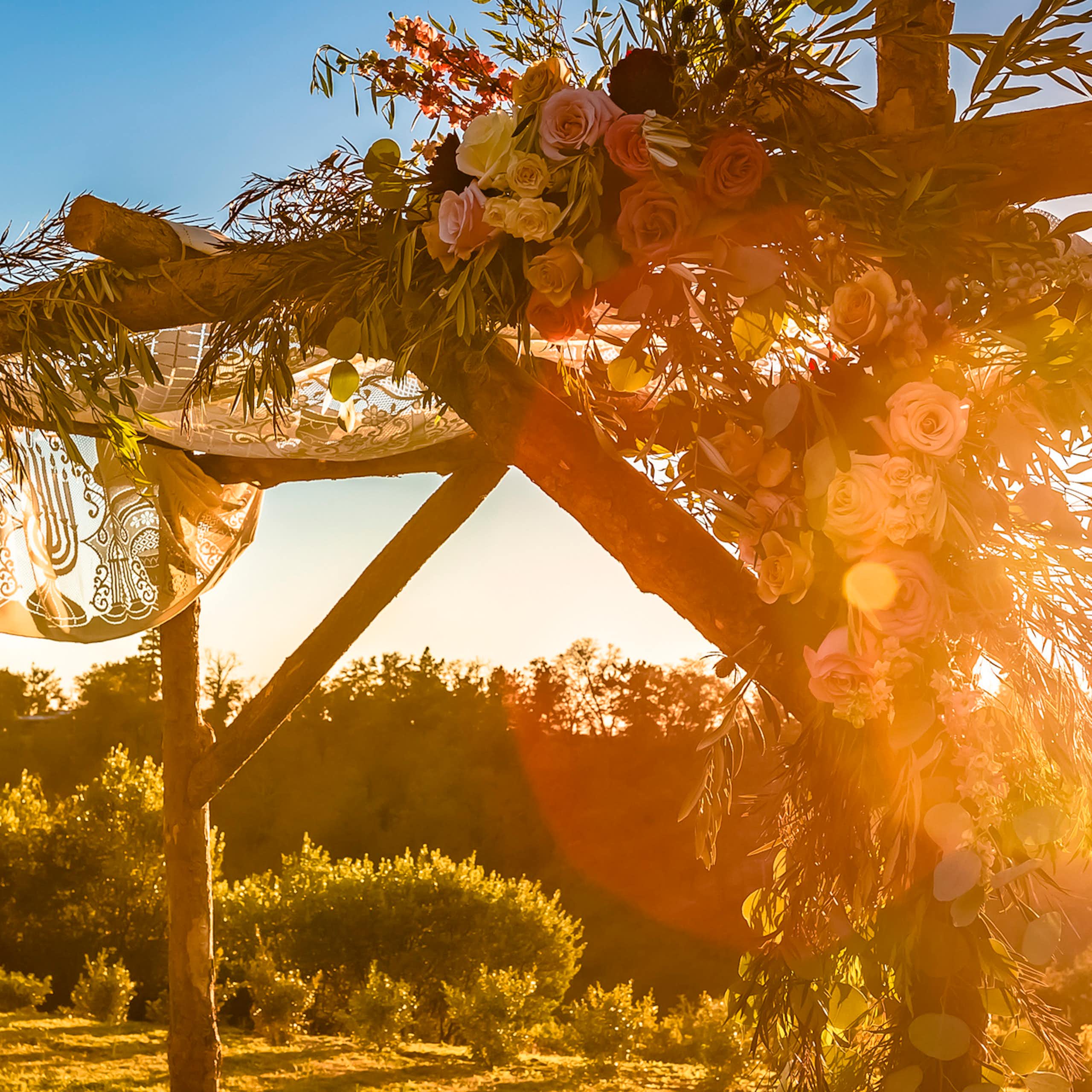 The sun begins to set hazily behind a simple wooden canopy adorned with flowers.