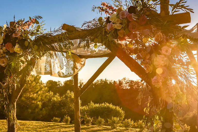 The sun begins to set hazily behind a simple wooden canopy adorned with flowers.