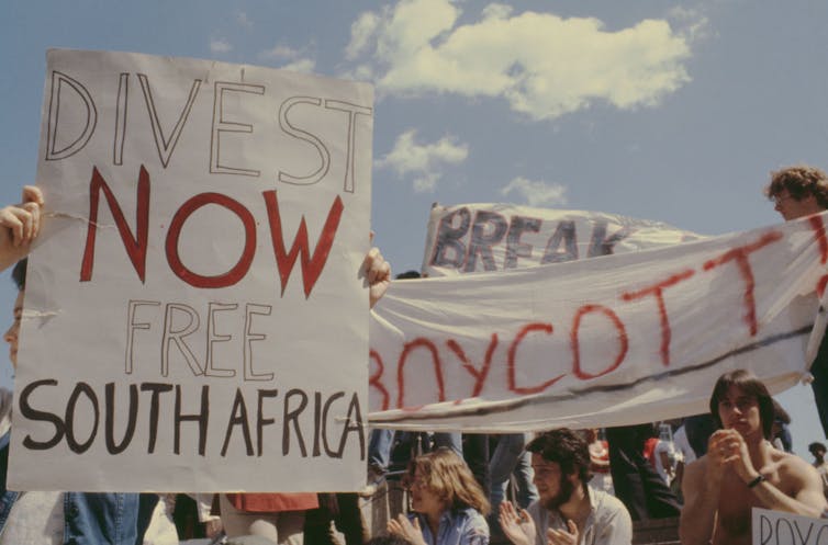 Students hold signs reading “Divest now: Liberate South Africa” and “BOYCOTT.”