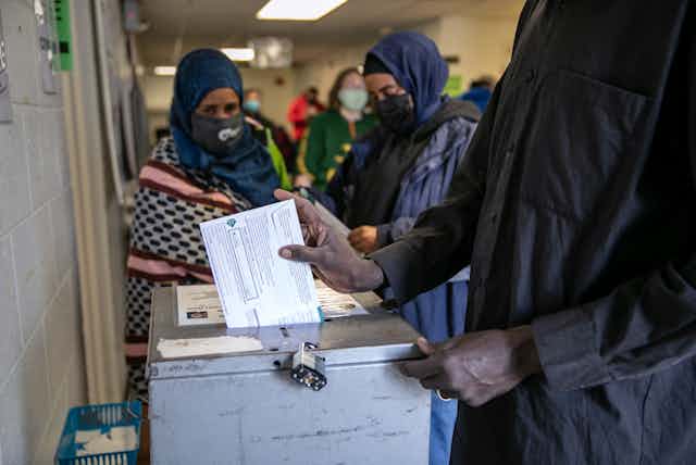 Three women wearing head scarves and masks, at a voting station.