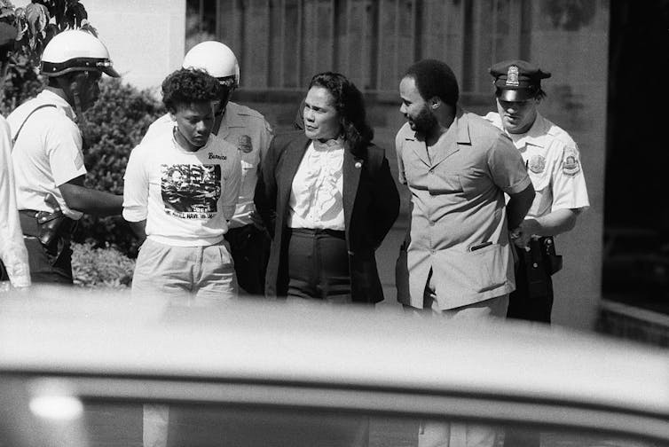 Police handcuff two Black women and a Black man.