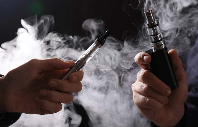 Two hands holding e-cigarettes
