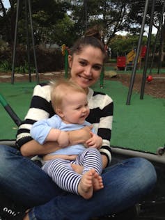 A mother at a playground with a baby in her lap.