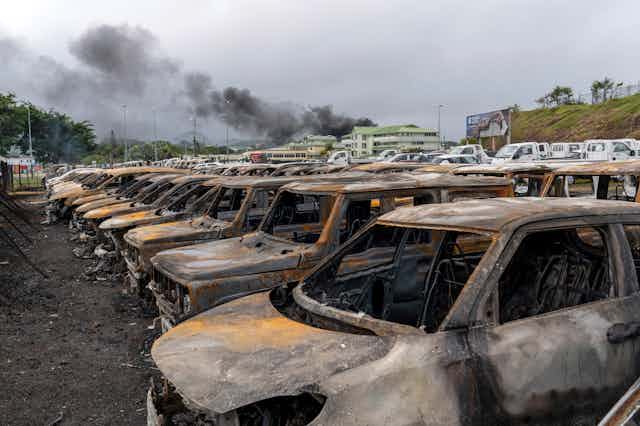Line of burnt-out cars with smoke rising in the background