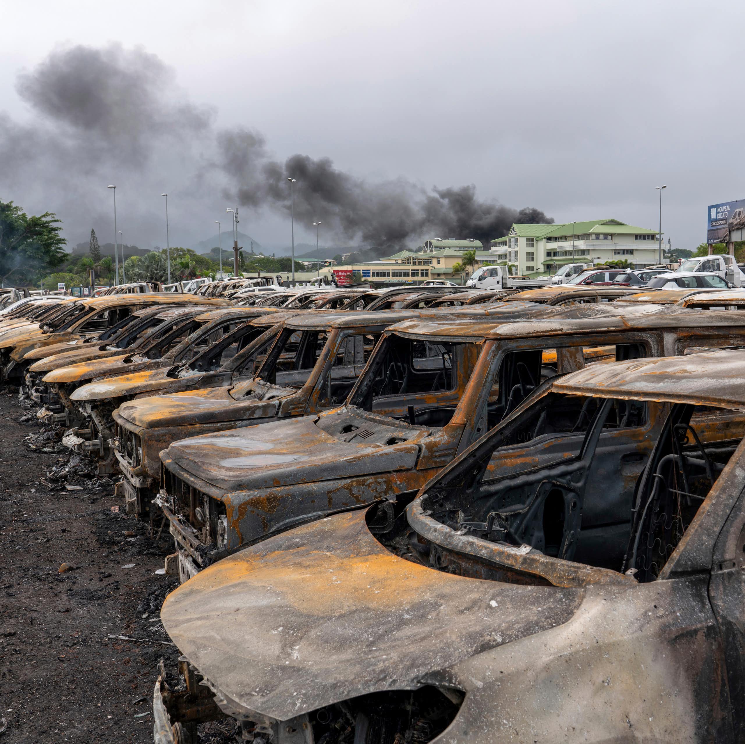 Line of burnt-out cars with smoke rising in the background