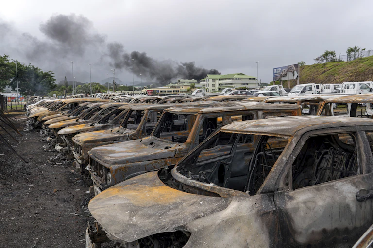Line of burnt-out cars with smoke rising in the background