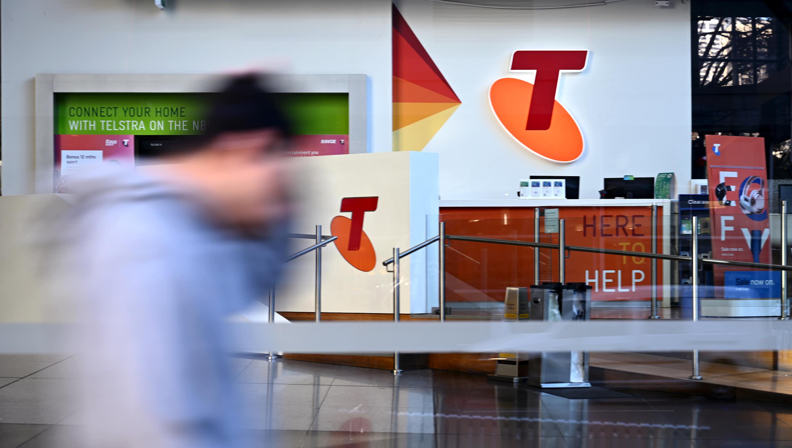 Blurred man seen walking in front of a large Telstra shop