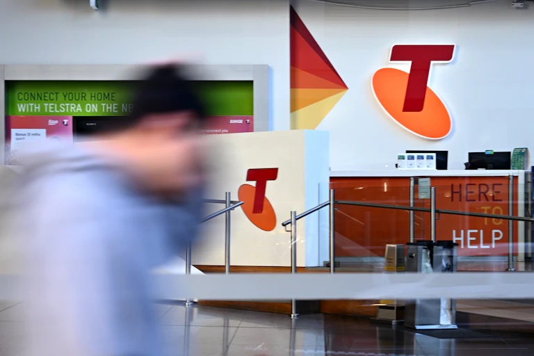 Blurred man seen walking in front of a large Telstra shop