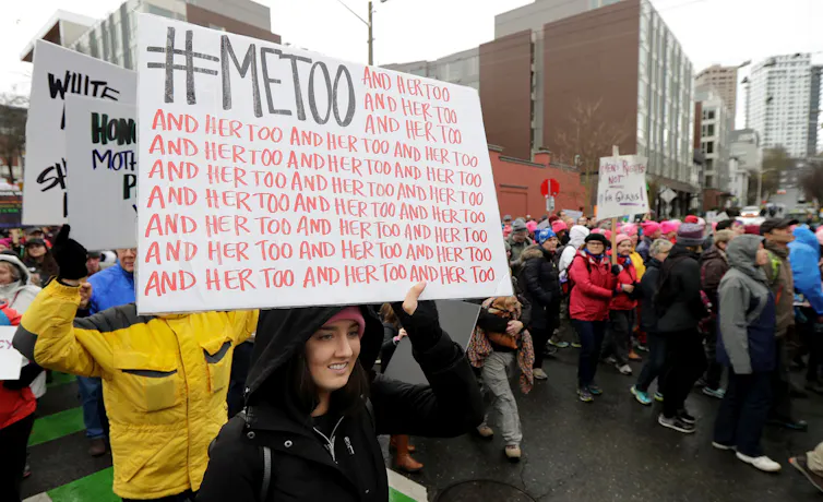 A march; a woman holds a sign saying 'me too, and her too and her too'