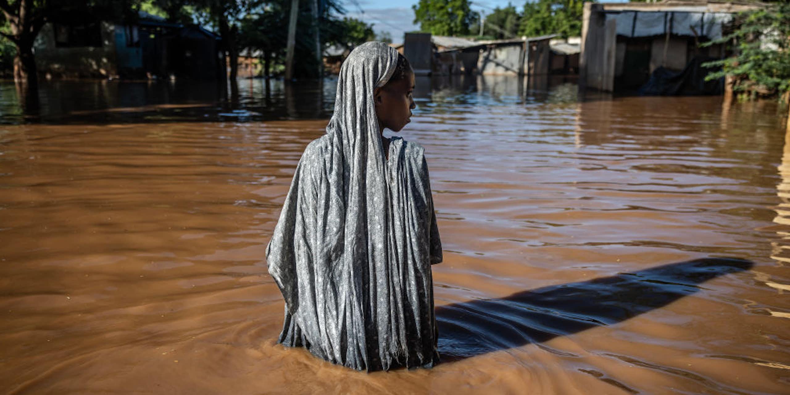 A solitary woman surrounded by waist deep flood water in flood waters look to one side.
