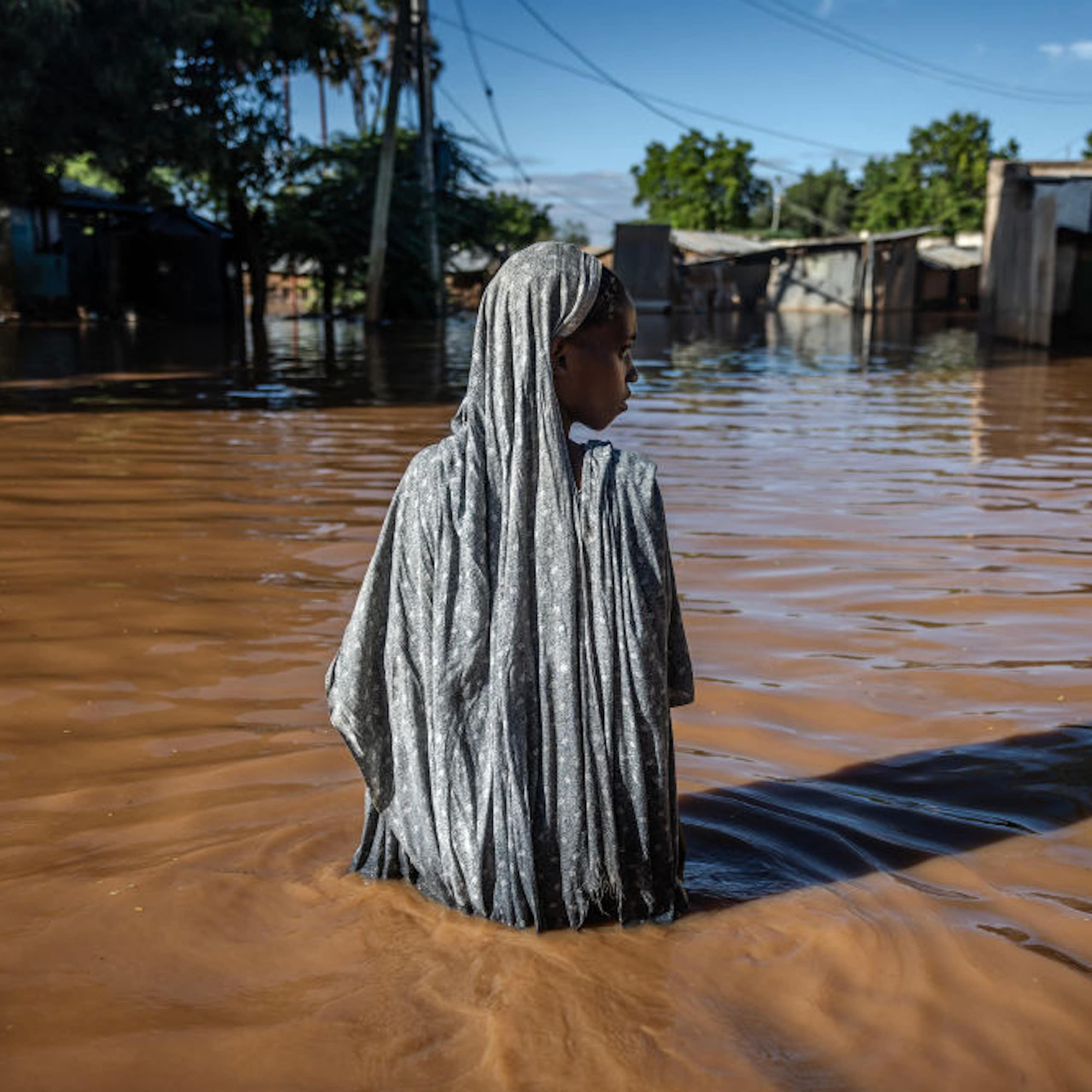 A solitary woman surrounded by waist deep flood water in flood waters look to one side.