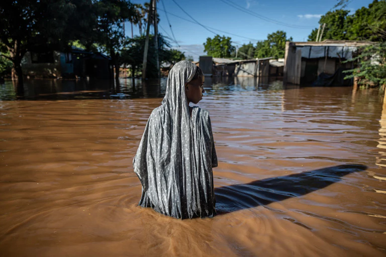 A solitary woman surrounded by waist deep flood water in flood waters look to one side.