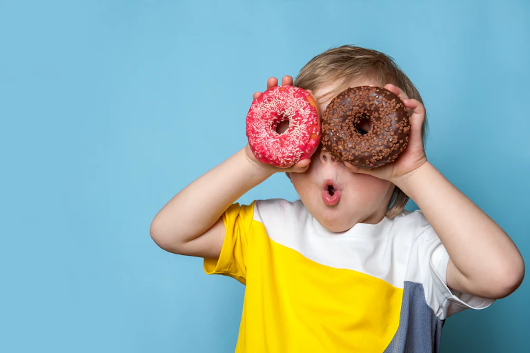 small child holds iced donuts over eyes and makes funny face