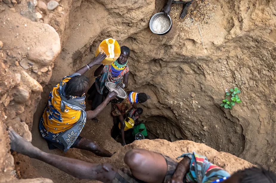 Several people going down a deep hand dug well with pots and pans and other water containers