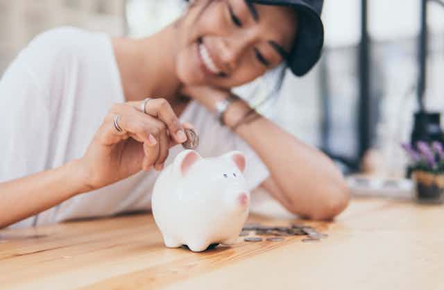 Smiling young woman inserts a coin into a piggy bank