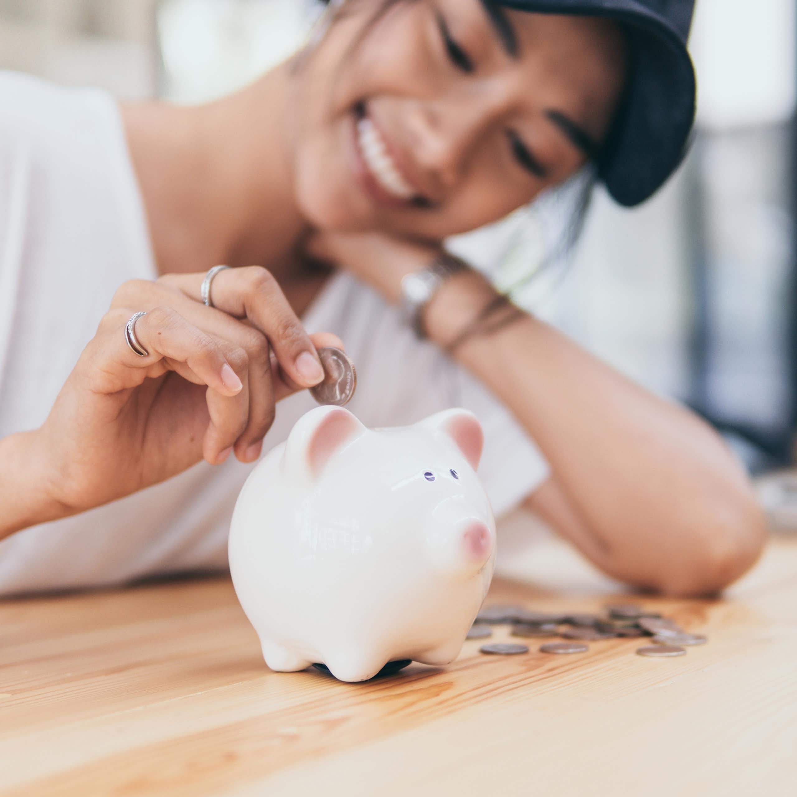 Smiling young woman inserts a coin into a piggy bank