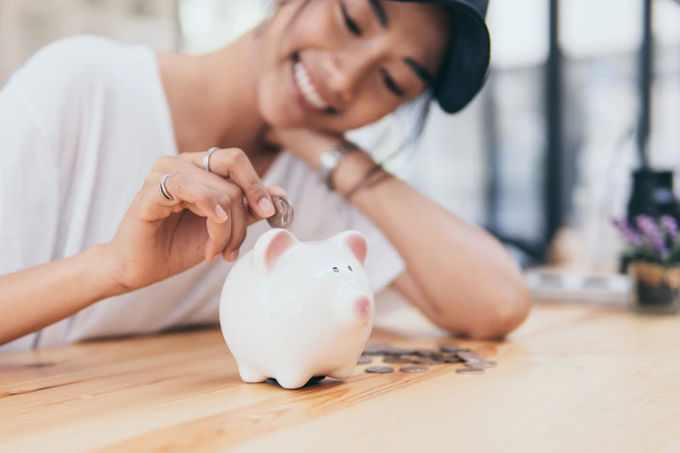Smiling young woman inserts a coin into a piggy bank