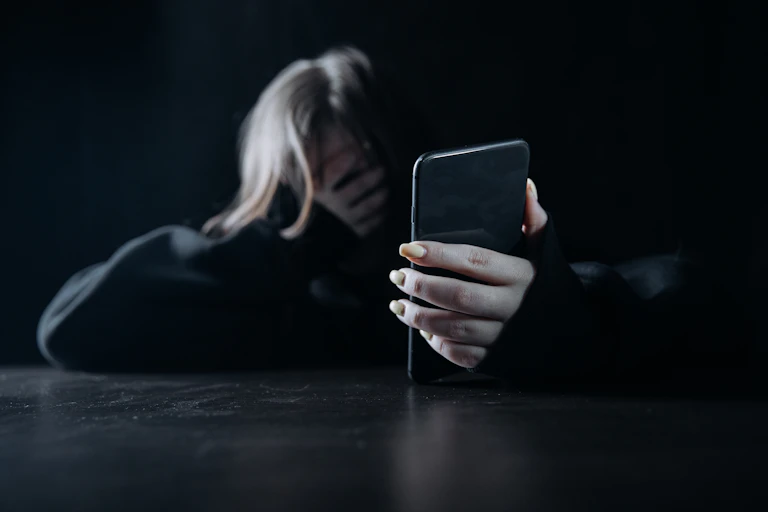 a woman places a hand across her face while she holds up a mobile phone