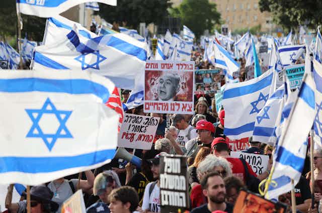 Israelis march with flags and banners with protests slogans in Hebrew.