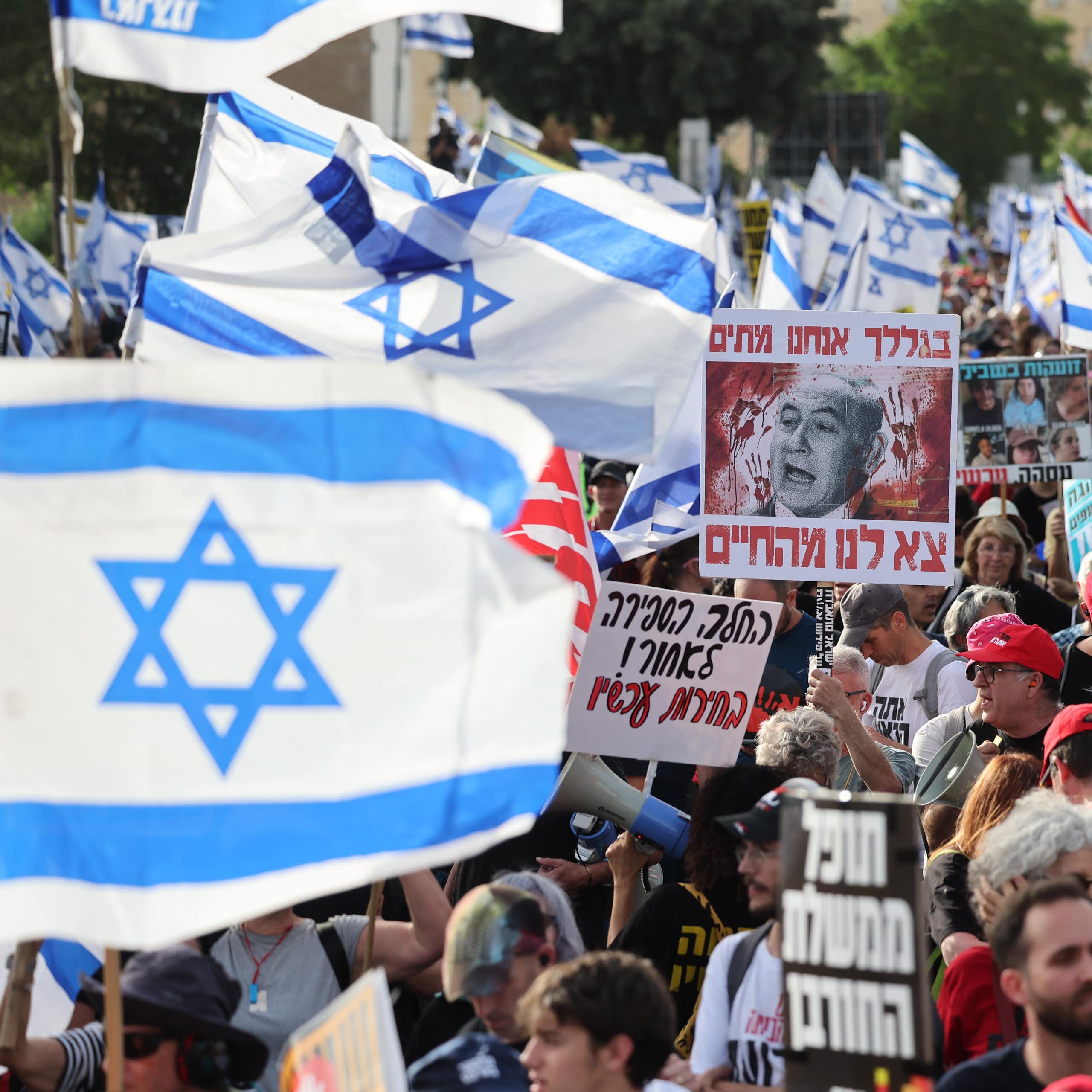 Israelis march with flags and banners with protests slogans in Hebrew.