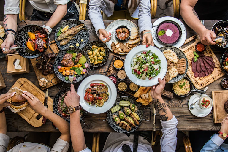 View from above of a table of various foods, with people seated all around.
