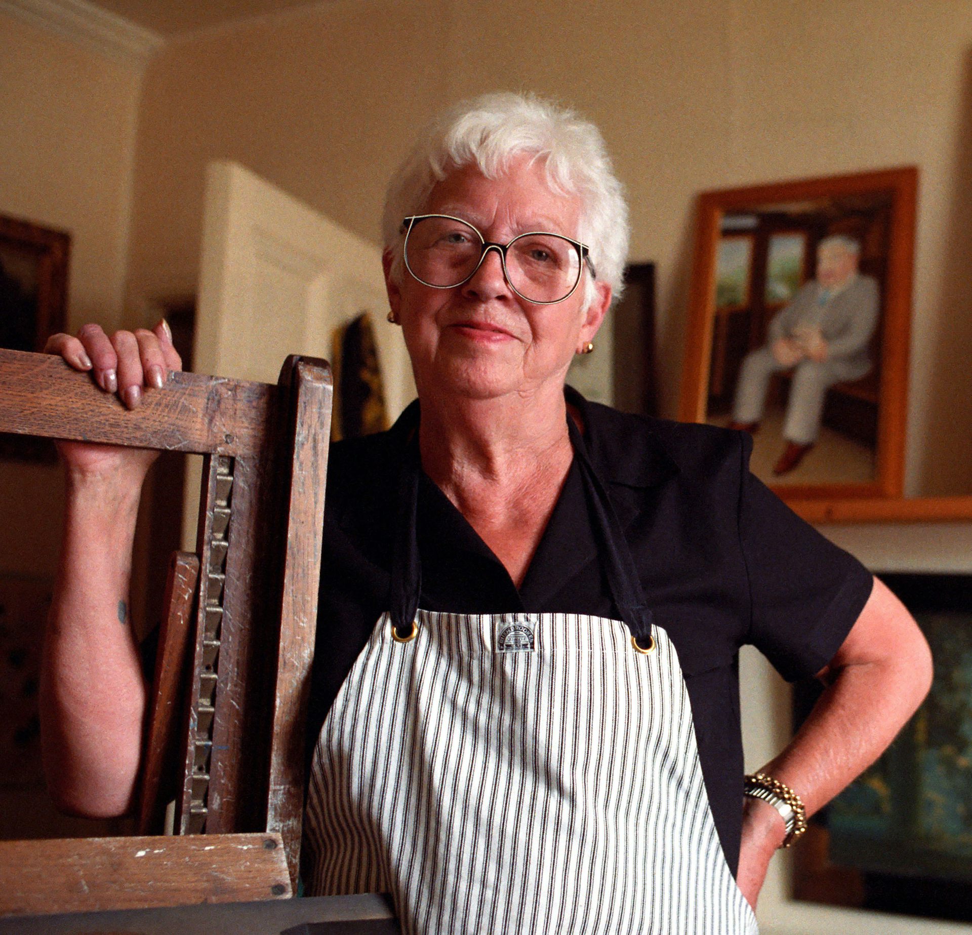A middle-aged woman stand in her art studio with her work in the background.
