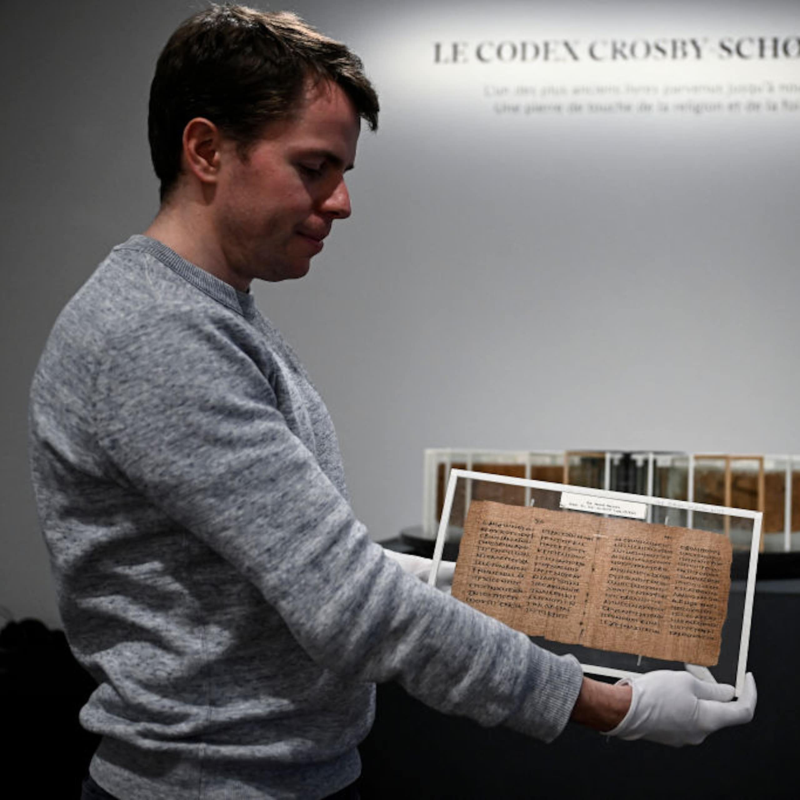 A man holds a yellowed manuscript with gloved hands.