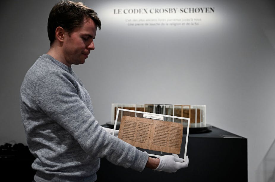 A man holds a yellowed manuscript with gloved hands.