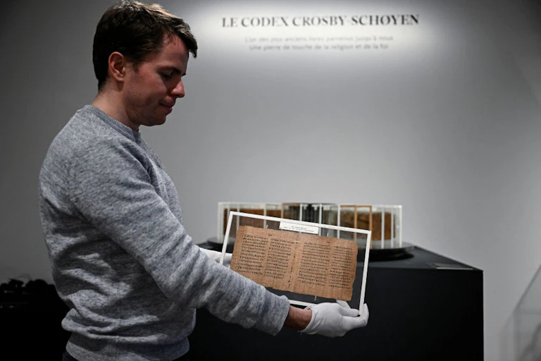 A man holds a yellowed manuscript with gloved hands.