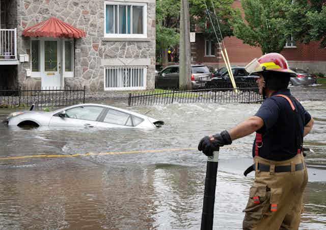 Un pompier se tient en marge d'une rue inondée