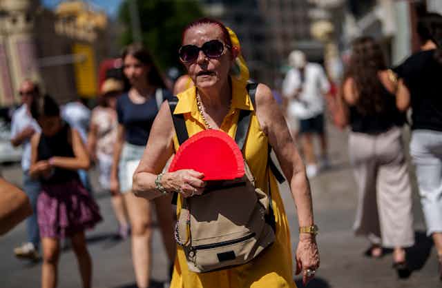 An older woman in Spain sweats as she waves a fan in the heat.