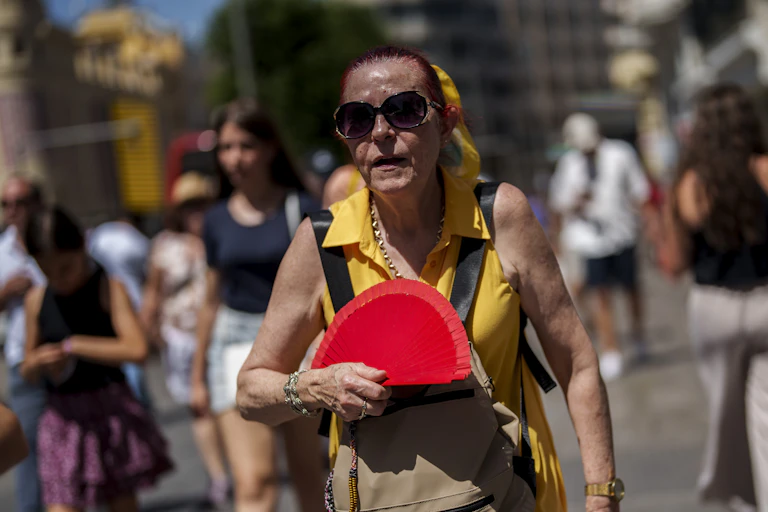 An older woman in Spain sweats as she waves a fan in the heat.