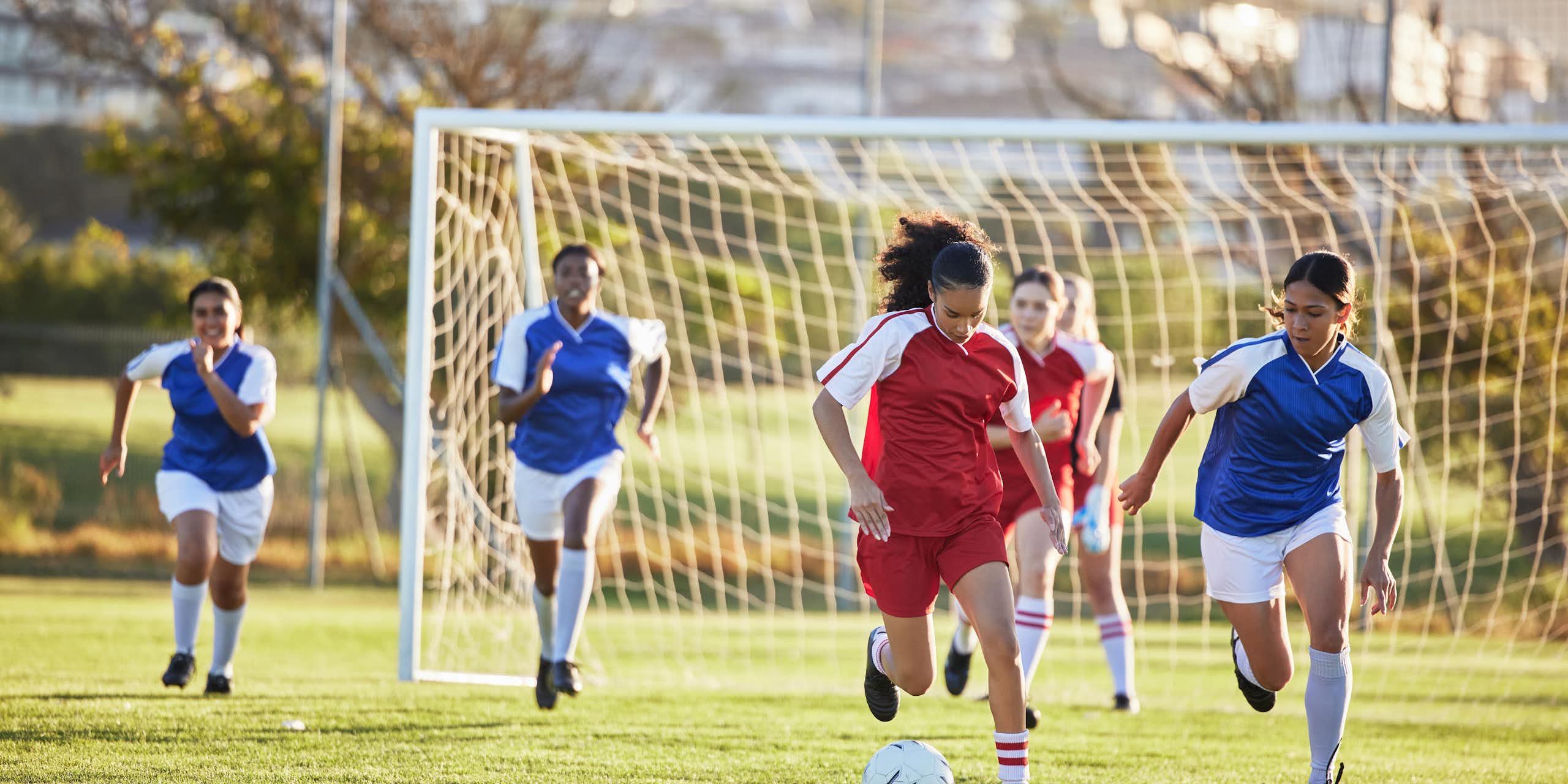 Sur un terrain de football, deux équipes de foot féminines s'affrontent.