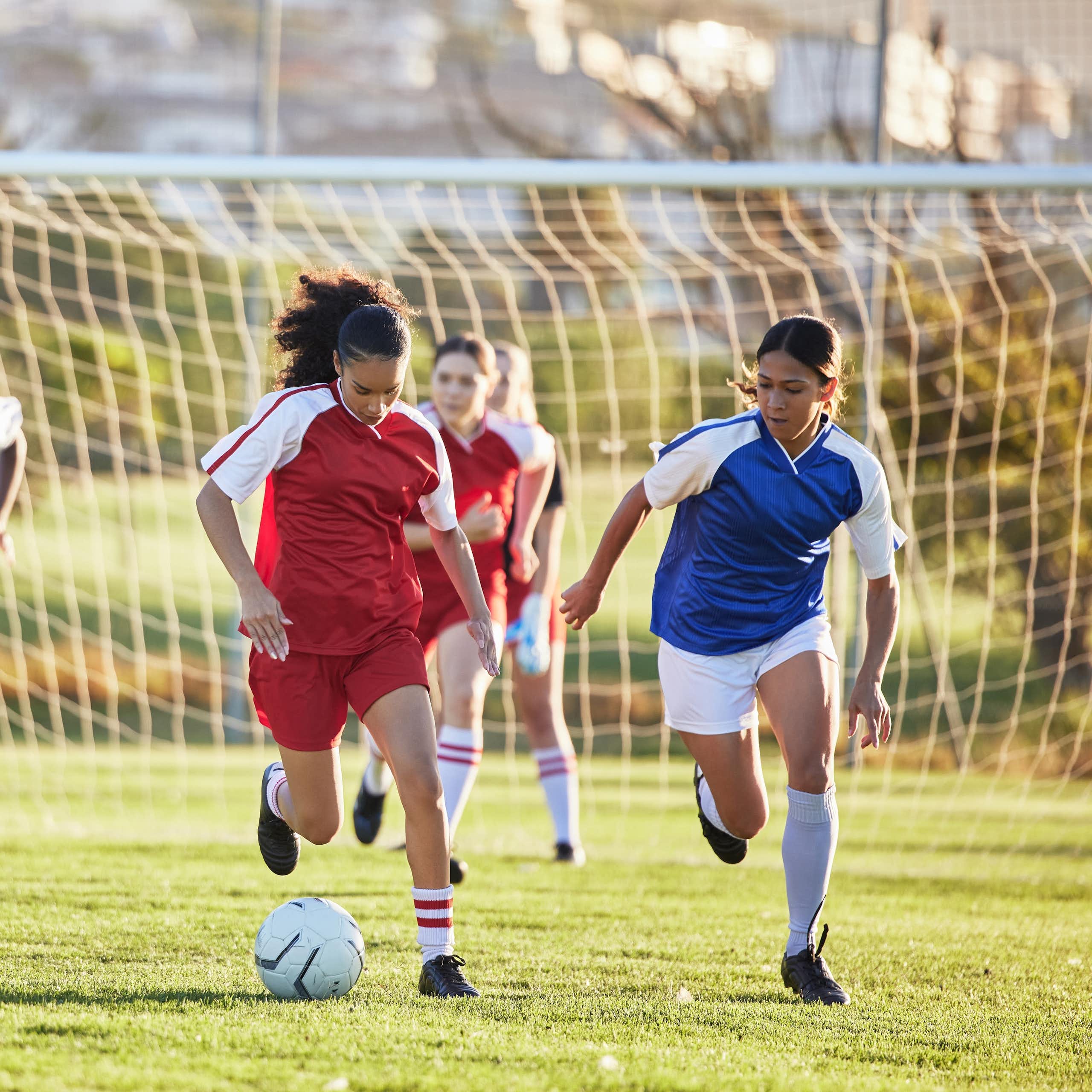 Sur un terrain de football, deux équipes de foot féminines s'affrontent.