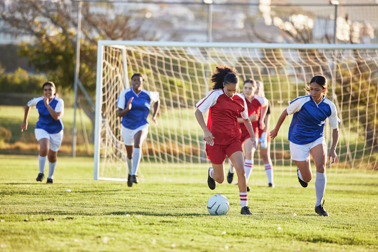 Sur un terrain de football, deux équipes de foot féminines s'affrontent.