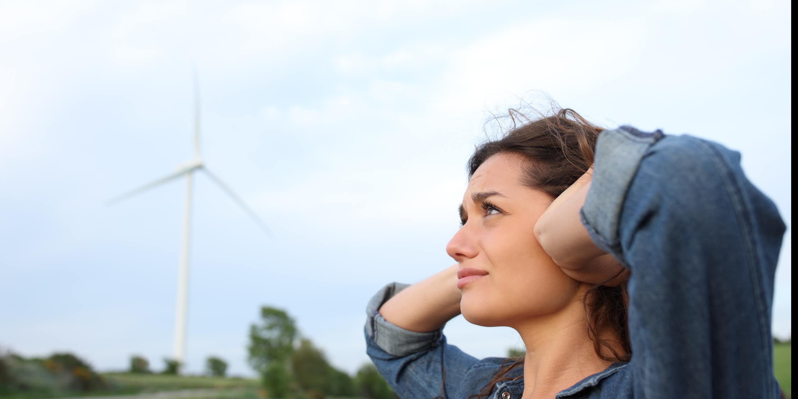 Femme se couvrant les oreilles à proximité d'une éolienne