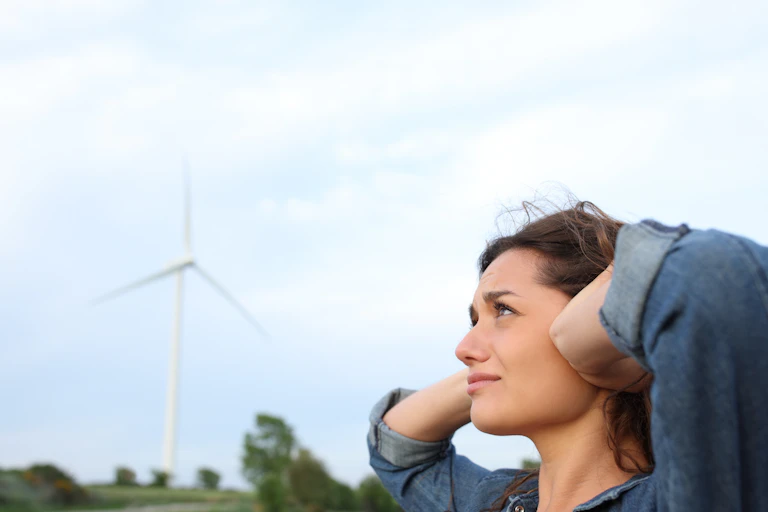 Femme se couvrant les oreilles à proximité d'une éolienne